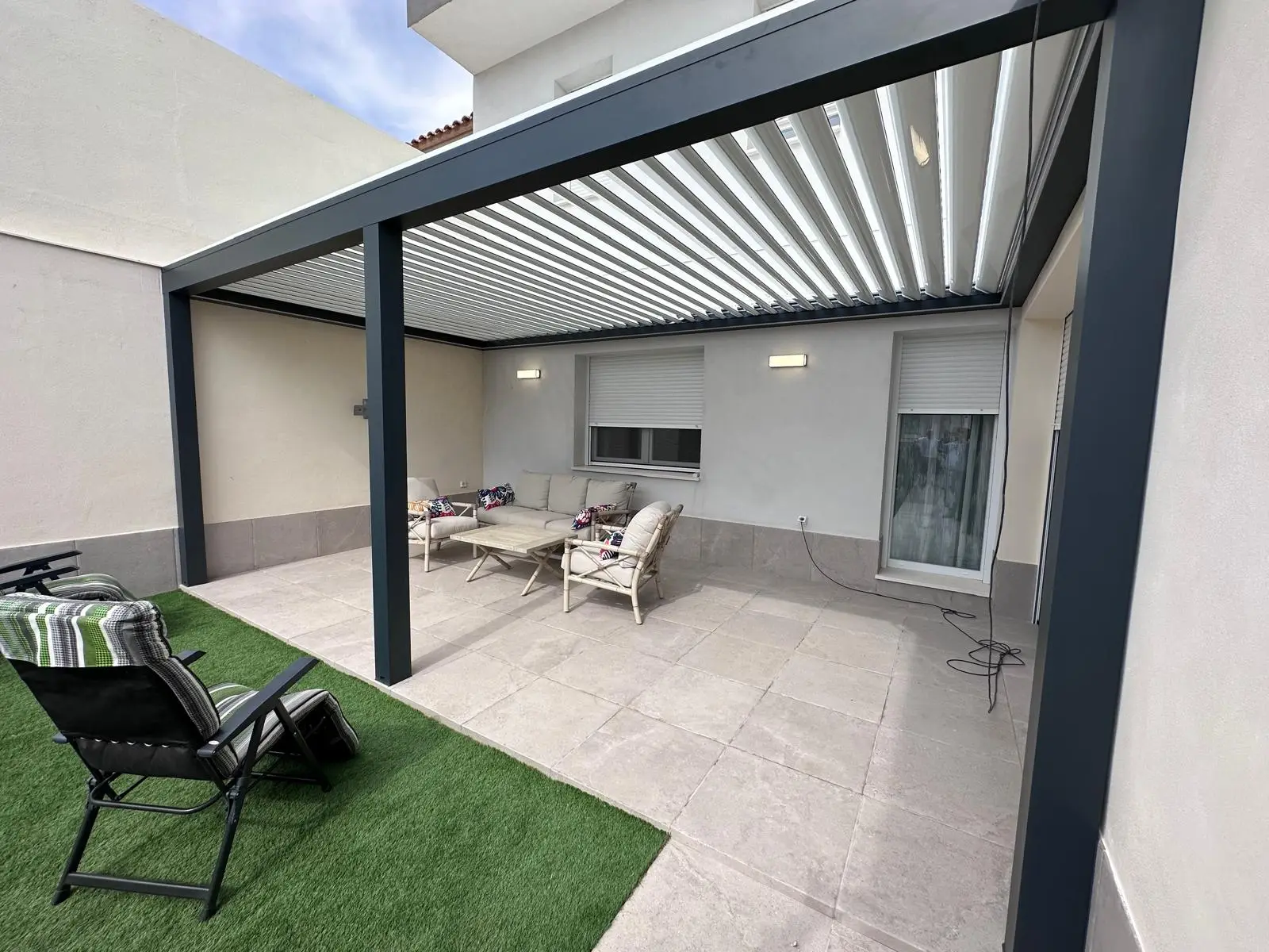 Anthrazitgraue bioklimatische Pergola mit drehbaren Lamellen über einer Sitzecke